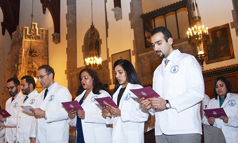 A group of people in white coats taking part in a graduation ceremony