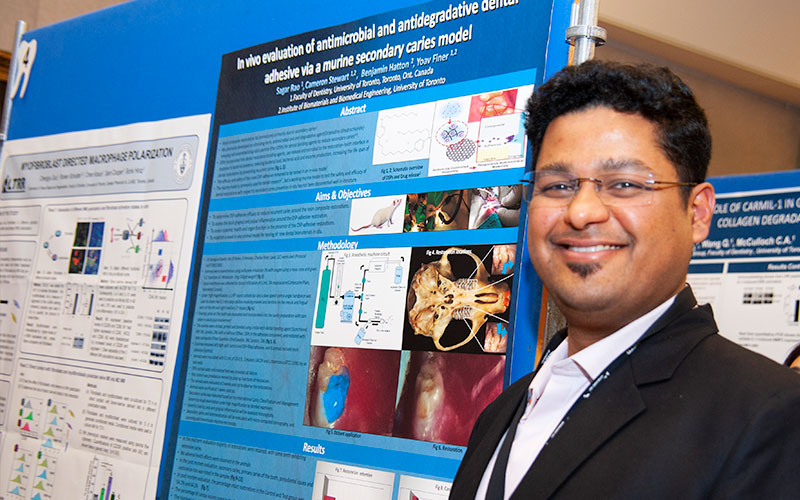 A student standing smiling next to their research poster