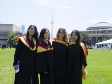four femaie students in gowns stand on commons, CN tower in the background