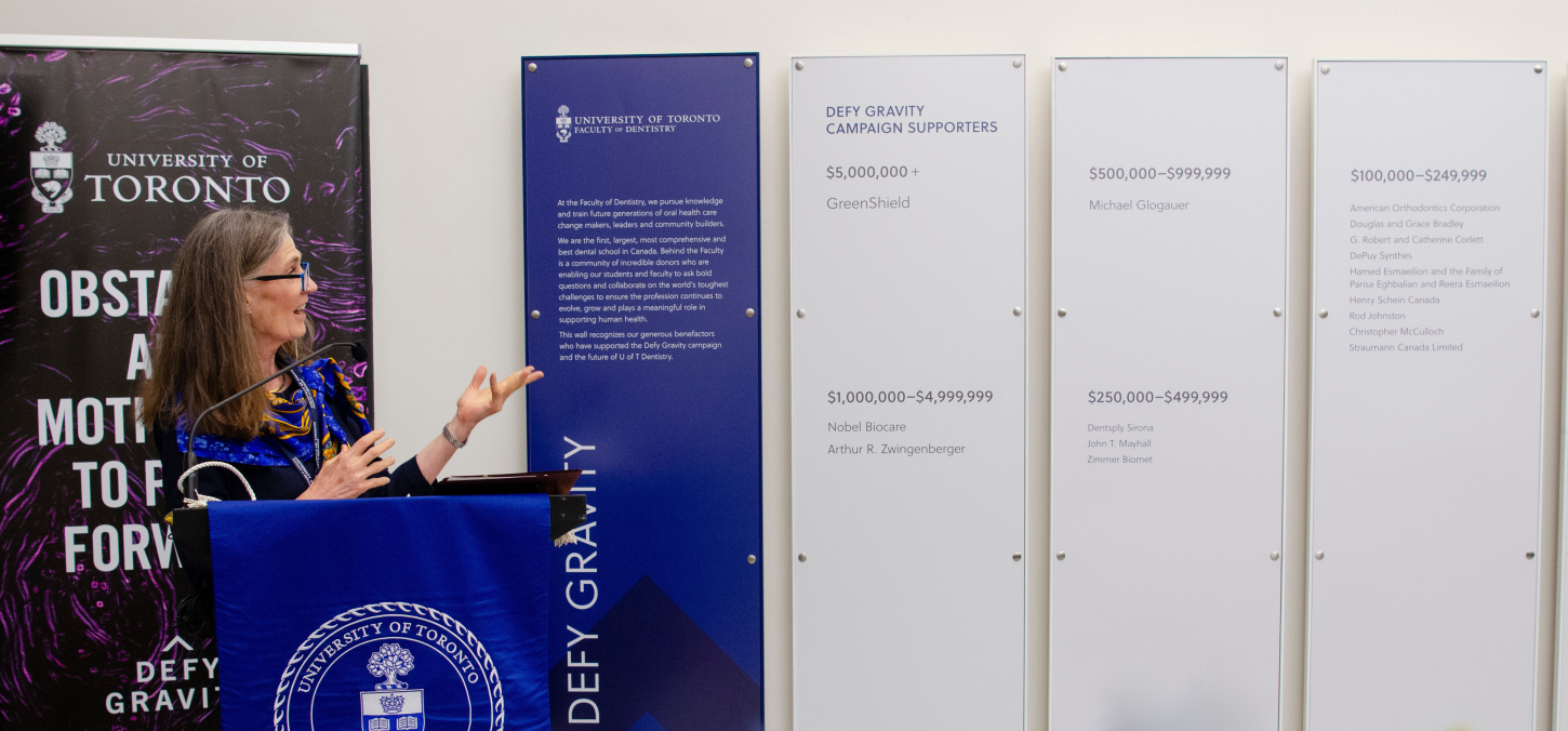 Photo of Elizabeth MacSween speaking next to the donor wall.
