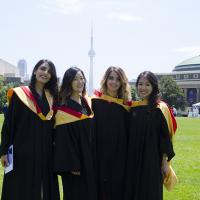 four femaie students in gowns stand on commons, CN tower in the background